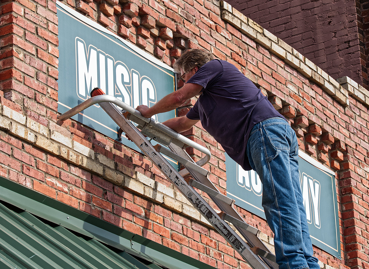 Bill Burtton removes the sign from the Espinoza Music Academy in downtown Mineola so that it can be repainted.